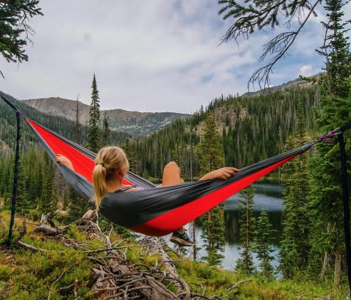 Woman reclining in a hammock beside a lake surrounded by pine trees